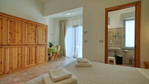A bedroom with a large bed, wooden wardrobe, and a bathroom visible through an open door.
