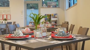 A dining area with tables set for two, featuring patterned napkins, clear glass vases, and a potted plant.