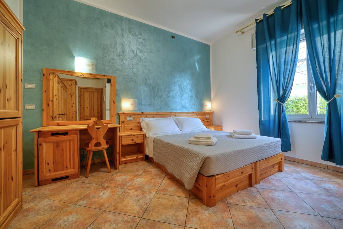 A bedroom with a wooden bed, a desk, a chair, and a mirror.