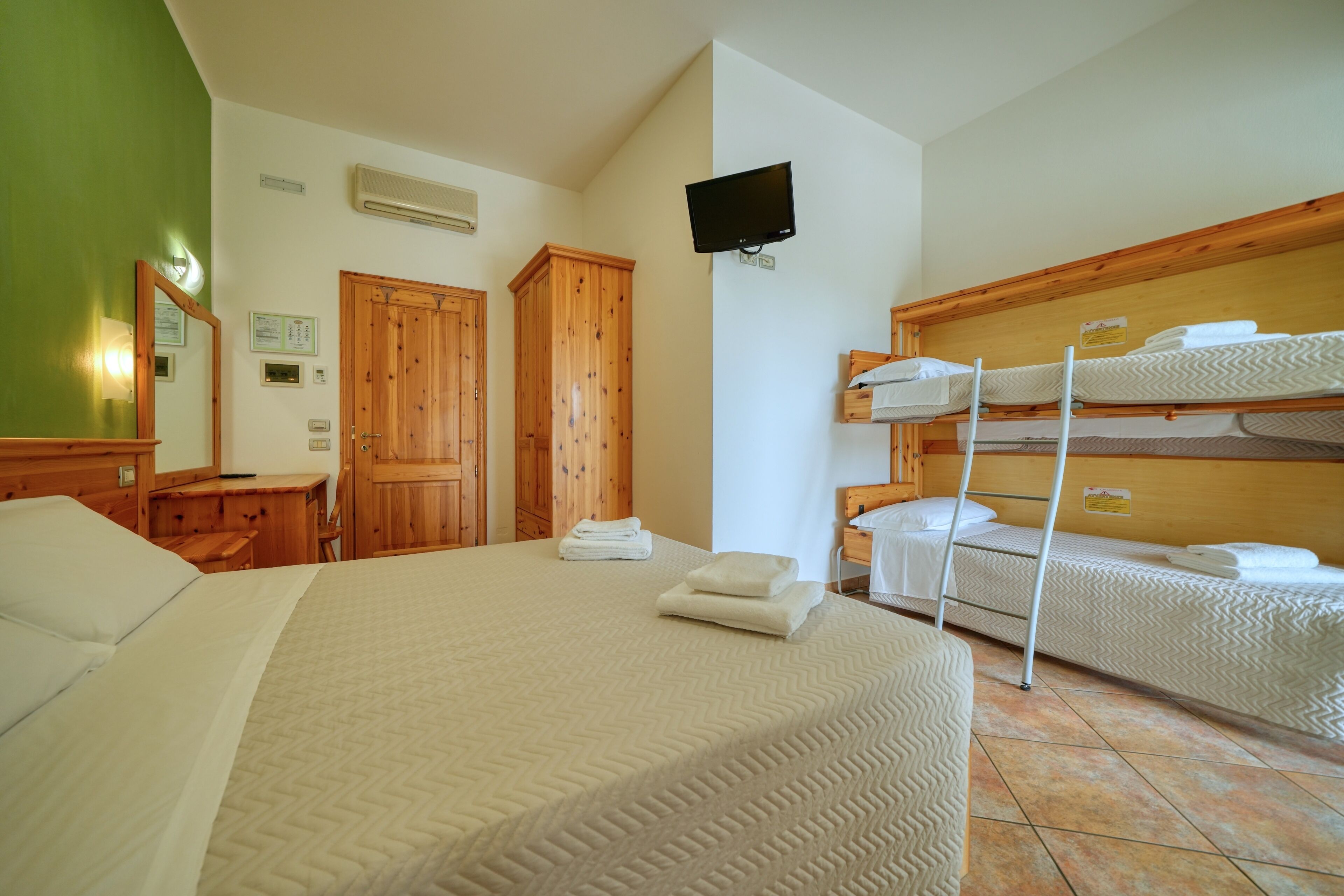 A hotel room with a large bed, a bunk bed, wooden furniture, and a flat-screen TV.