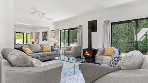 A modern living room with a glass coffee table, grey sofas, and a wood-burning stove. - Jasmine House - Pet Friendly with Swimming Pool (Berry)