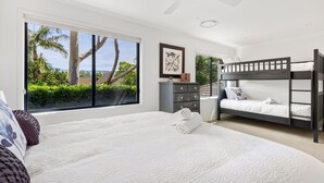 A bedroom with a large bed, a bunk bed, a dresser, and a window with a view of palm trees and greenery. - Jasmine House - Pet Friendly with Swimming Pool (Berry)