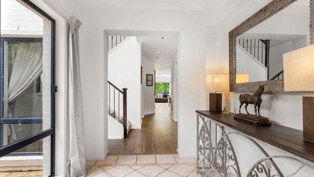A hallway with a staircase leading to a living area, a large mirror, and a lamp on a console table. - Jasmine House - Pet Friendly with Swimming Pool (Berry)