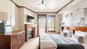 A bedroom with a large bed, a fireplace, a TV, and a mountain mural on the wall.