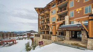 A multi-story hotel with a stone facade, balconies, and a ski resort sign.
