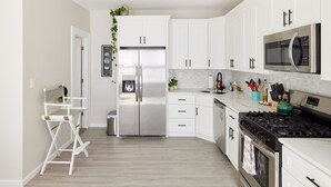 A modern kitchen with white cabinets, stainless steel appliances, and a wooden floor. - Cozy 3 bedroom home by the beach with designated work space (Long Beach)
