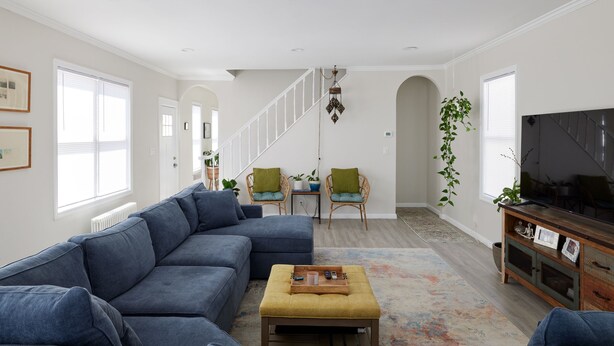 A modern living room with a sectional sofa, a coffee table, and a TV on a wooden cabinet. There is a staircase leading to an upper level, and a plant hanging from the ceiling. - Cozy 3 bedroom home by the beach with designated work space (Long Beach)