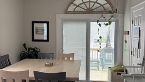 A dining area with a wooden table and chairs, a ceiling fan, and a view of the outdoors through a glass door. - Cozy 3 bedroom home by the beach with designated work space (Long Beach)