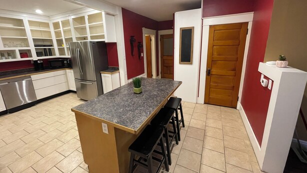 Una cocina moderna con armarios blancos, encimera de granito, electrodomésticos de acero inoxidable y una isla central con taburetes de bar.