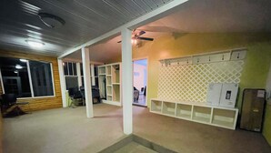 Un pasillo con piso alfombrado, columnas blancas, ventilador de techo y pared de celosías blancas con estantes.