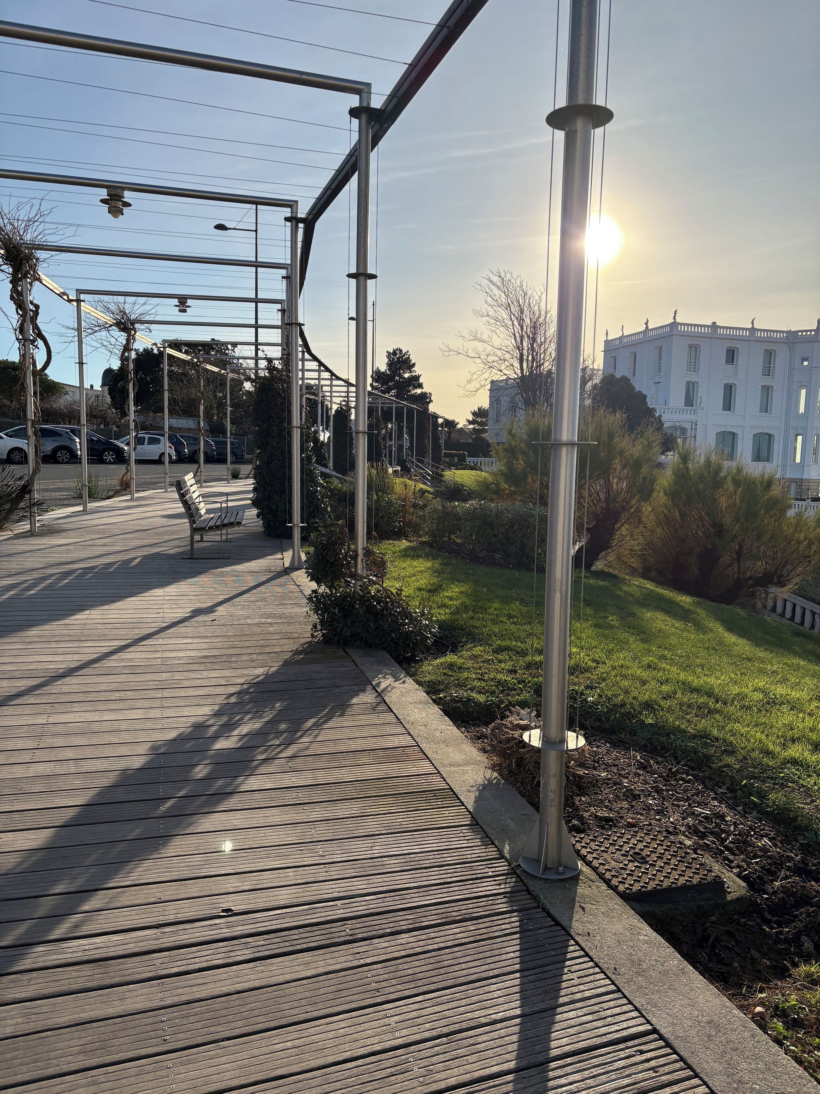 Un pontile in legno con ringhiere in metallo, una panchina e una zona verde con un edificio sullo sfondo.