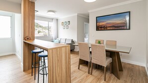 A modern kitchen with a wooden island, bar stools, and a dining area with chairs and a table. - WI-FI 500MB | 50” Smart TV | Swimming Pool #CA67 (Florianópolis)
