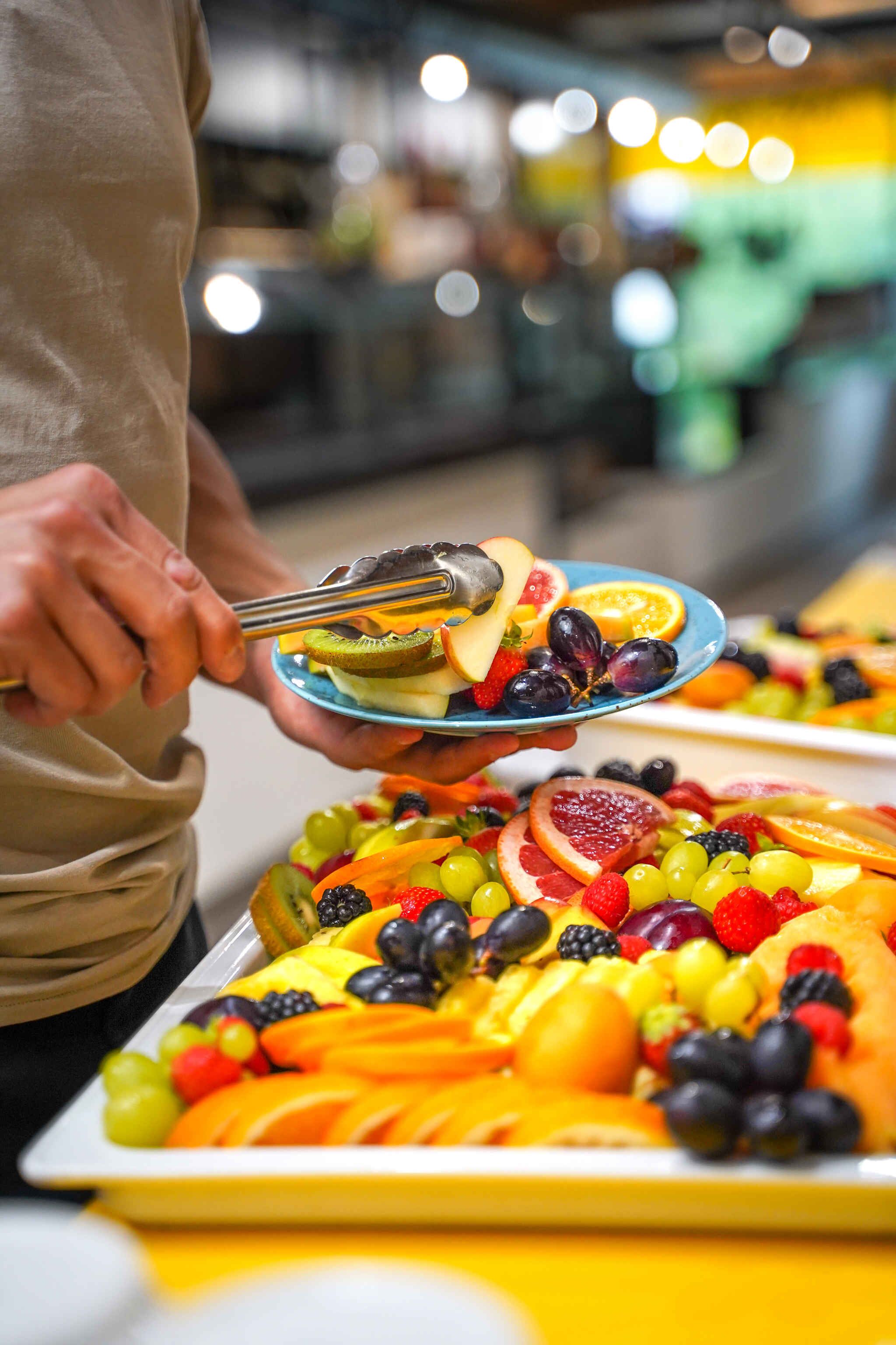 A person holding a plate with various fruits.