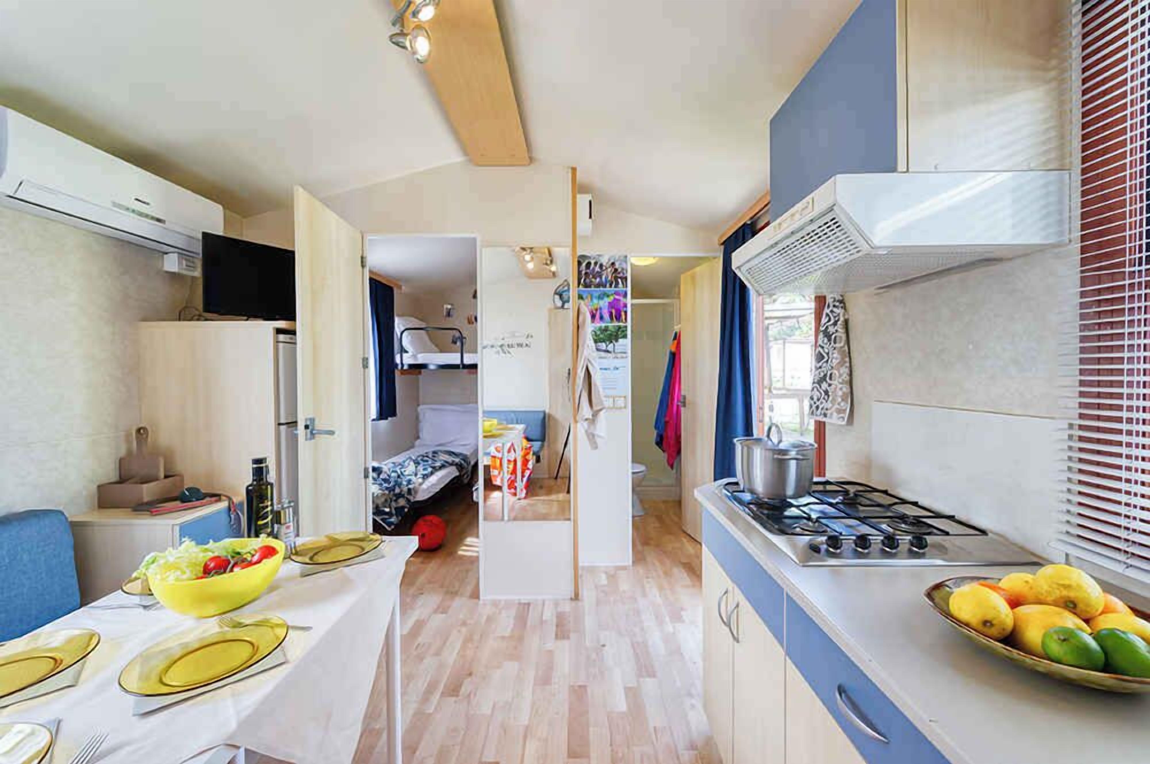 Een kleine keuken met een fornuis, een eethoek met een tafel gedekt voor twee personen, en een kleine koelkast.
