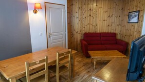 Une pièce avec un plancher en bois, une table à manger en bois avec des chaises, un canapé rouge, une petite table basse en bois et un téléviseur.
