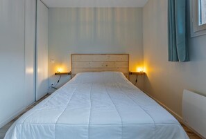 A bed with a wooden headboard, two bedside lamps, and a window with curtains.