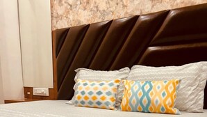 Una camera d'hotel con una coperta a motivi, due cuscini decorati, una testiera scura e una parete in marmo.