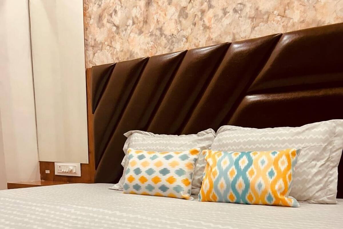 A hotel room with a patterned bedspread, two patterned pillows, a dark headboard, and a marble wall.