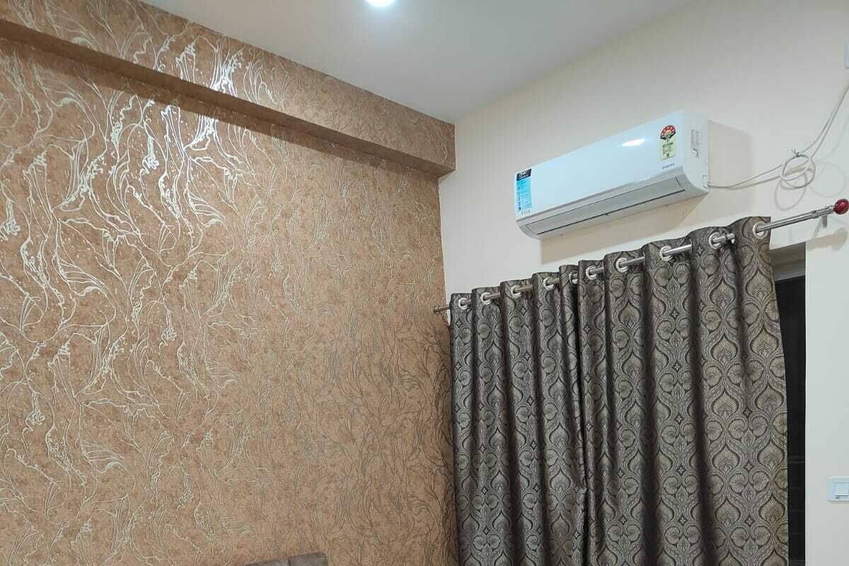 Un dormitorio con cama, cabecera, aire acondicionado y cortinas estampadas.
