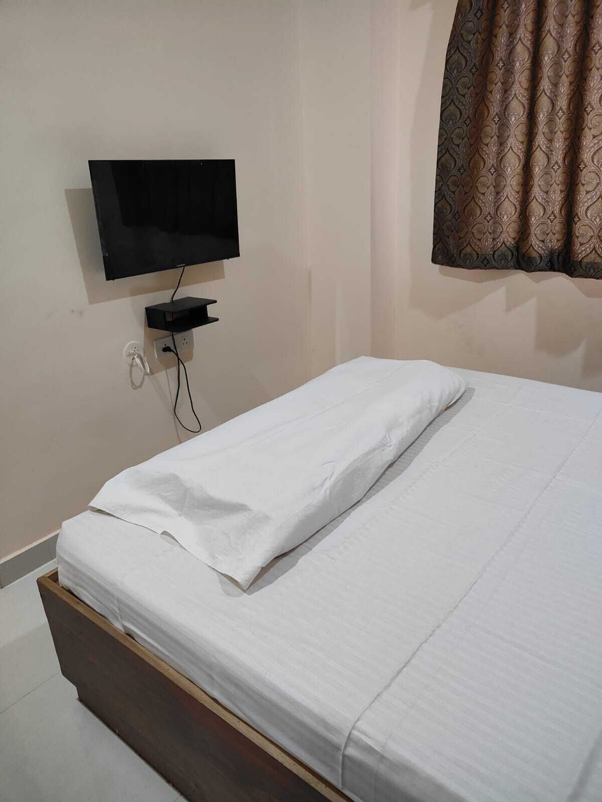A bedroom with a bed, a TV mounted on the wall, and a curtain.