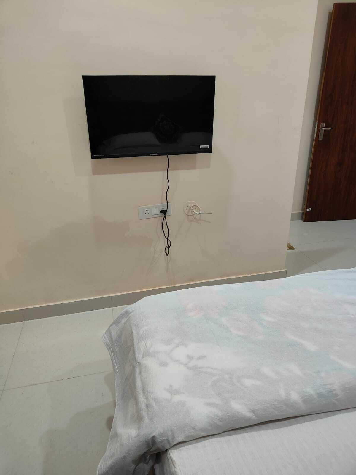 Un dormitorio con una cama, un televisor montado en la pared y una puerta de madera.