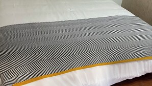 Ein ordentlich bezogenes Bett mit gemusterten Betttextilien, eine weiße Wand und ein Holzboden.