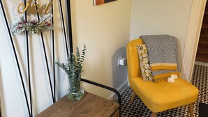 Ein Zimmer mit einem Holztisch, einem gelben Sessel, einem an der Wand befestigten Garderobehaken und einem dekorativen Wandbild.
