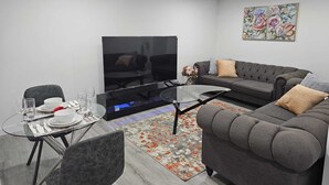 A modern living room with a sofa, a glass coffee table, a dining table set with plates and glasses, and a flat-screen TV. - Contemporary Two Bedroom Basement Suite. (Edmonton)