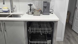A modern kitchen with white cabinetry, a stainless steel sink, and a built-in dishwasher. - Contemporary Two Bedroom Basement Suite. (Edmonton)