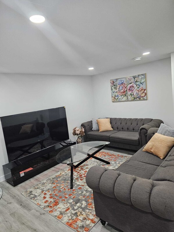 Ein modernes Wohnzimmer mit Flachbildfernseher, Glastisch und grauem Sofa.