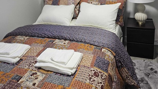 A neatly made bed with a patterned quilt and pillows, a bedside lamp, and two framed artworks on the wall. - Contemporary Two Bedroom Basement Suite. (Edmonton)