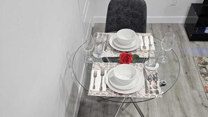 A dining area with a glass table set for two, featuring white plates, silverware, and a red rose centerpiece. - Contemporary Two Bedroom Basement Suite. (Edmonton)