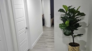 A hallway with white doors, a potted plant, and a trash bin. - Contemporary Two Bedroom Basement Suite. (Edmonton)