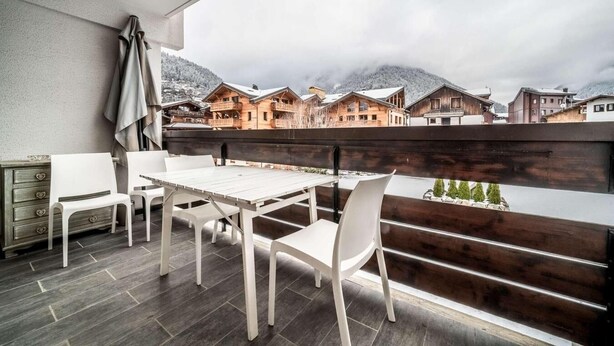 Ein Balkon mit Holzwertkasten, weißen Stühlen und einem Tisch.