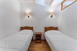 A small, clean room with two single beds, wooden headboards, and bedside tables.