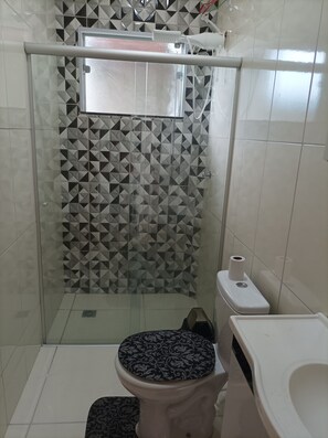 A bathroom with a geometric patterned shower wall, a toilet with a patterned seat, and a hand dryer.
