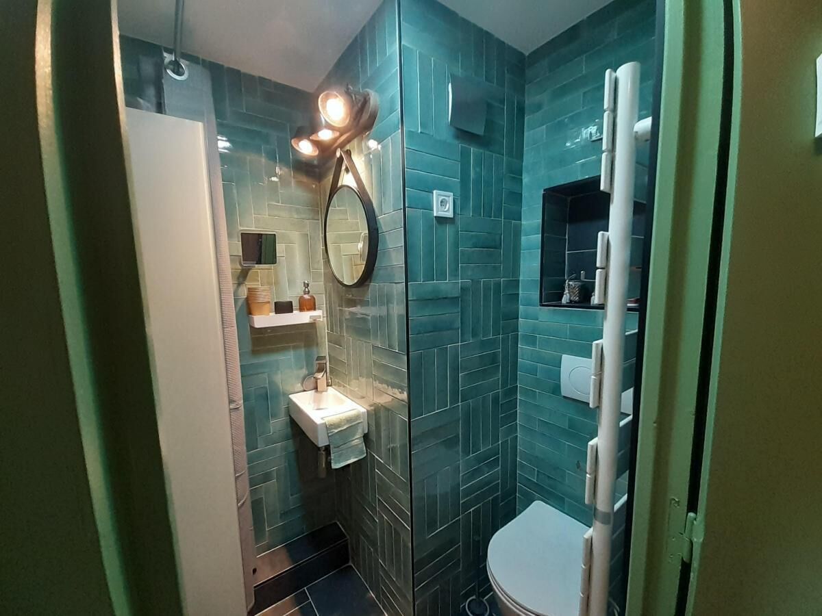 A bathroom with teal tiles, a white sink, a mirror, and a toilet.
