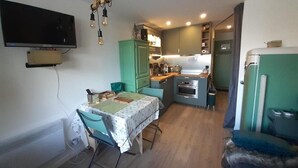 A compact kitchen with a dining area, a TV mounted on the wall, and a small refrigerator.