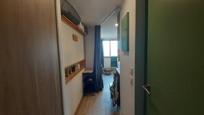 A narrow hallway with a wooden door on the left, a green door on the right, and a window at the end.