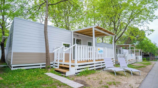 A mobile home with a porch and deck, surrounded by trees.