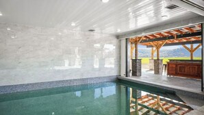 Una piscina interior con agua cristalina, suelo de baldosas y vistas al exterior a través de un ventanal.