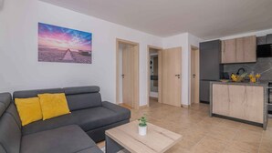 A modern living room with a gray sofa, a coffee table with a plant, and a kitchen area with wooden cabinets and a tiled backsplash. - Holiday apartment Apartment with heated pool and sea view (Klimno)