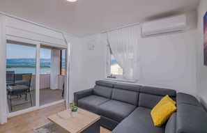 Un salon moderne avec un canapé gris, une petite table basse en bois et une vue sur un lac, visible à travers une porte-fenêtre coulissante.