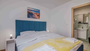 A hotel room with a bed, a nightstand, a bathroom with a sink and mirror, and a beach scene on the wall. - Holiday apartment Apartment with heated pool and sea view (Klimno)
