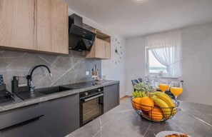 A modern kitchen with a marble countertop, a built-in oven, and a fruit basket with oranges and bananas.