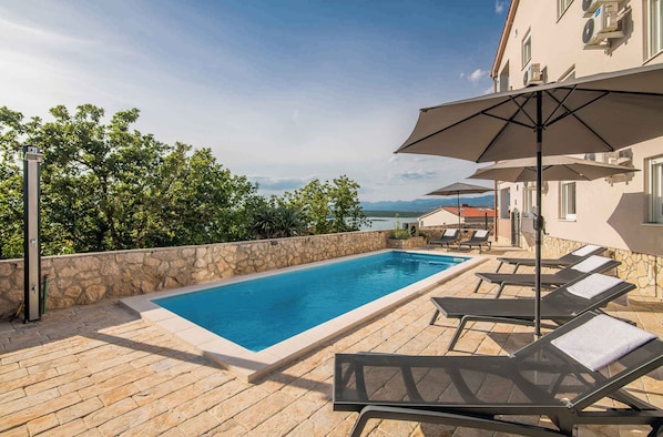 Une piscine entourée de chaises longues et de parasols, bordée de murs en pierre et offrant une vue sur les arbres et les montagnes.