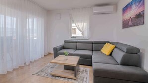 A modern living room with a grey sectional sofa, a wooden coffee table, and a yellow pillow. - Holiday apartment Apartment with heated pool and sea view (Klimno)