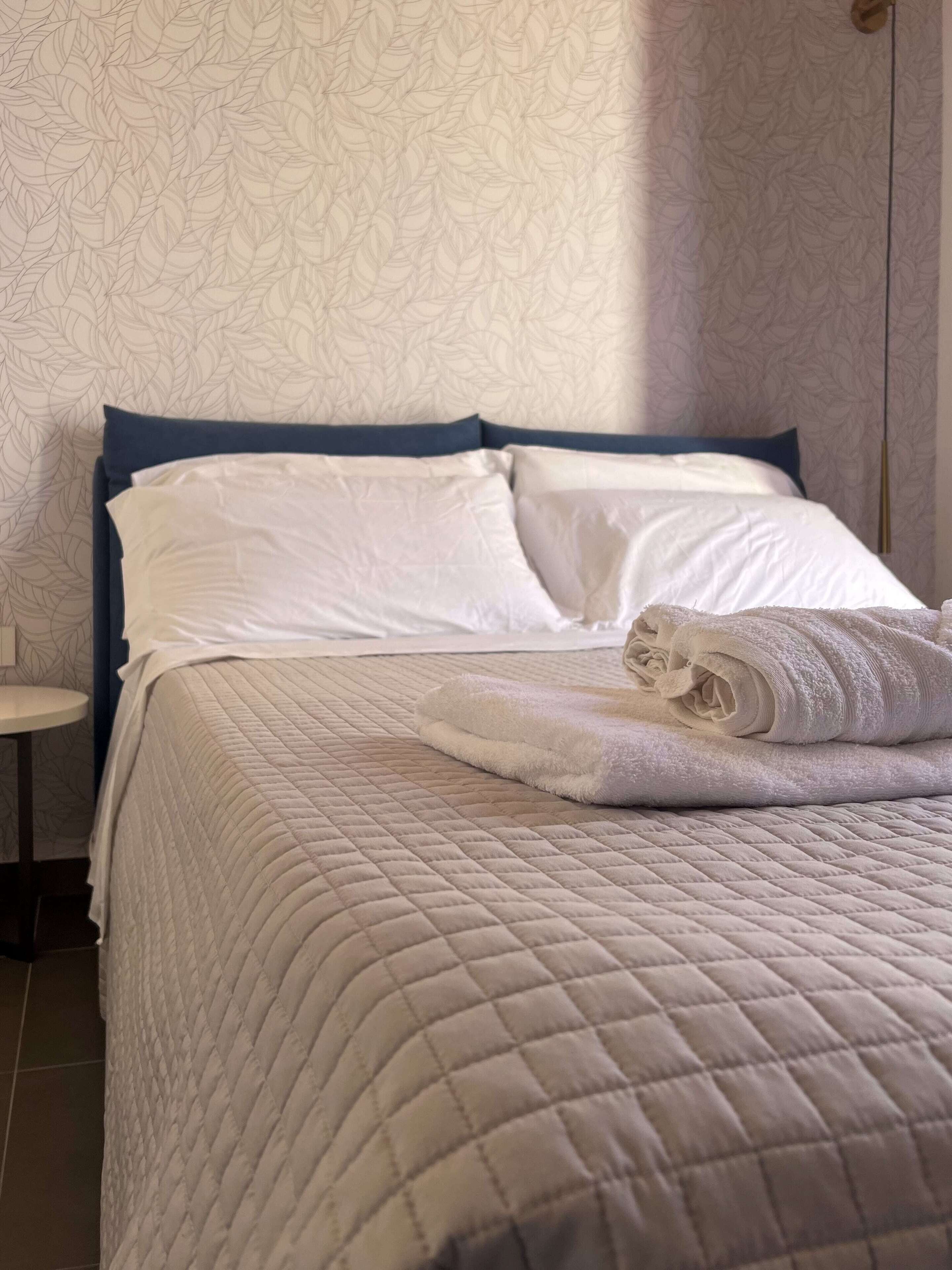Un lit bien fait, recouvert d’une courtepointe blanche matelassée, avec une serviette blanche pliée posée sur le dessus.