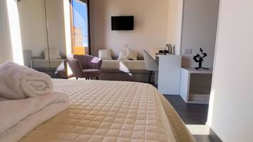 Una habitación de hotel moderna con una cama grande, zona de estar, televisor de pantalla plana y un escritorio pequeño.