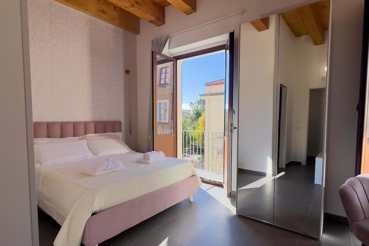 A bedroom with a bed, a sliding glass door leading to a balcony, and a view of the outside.